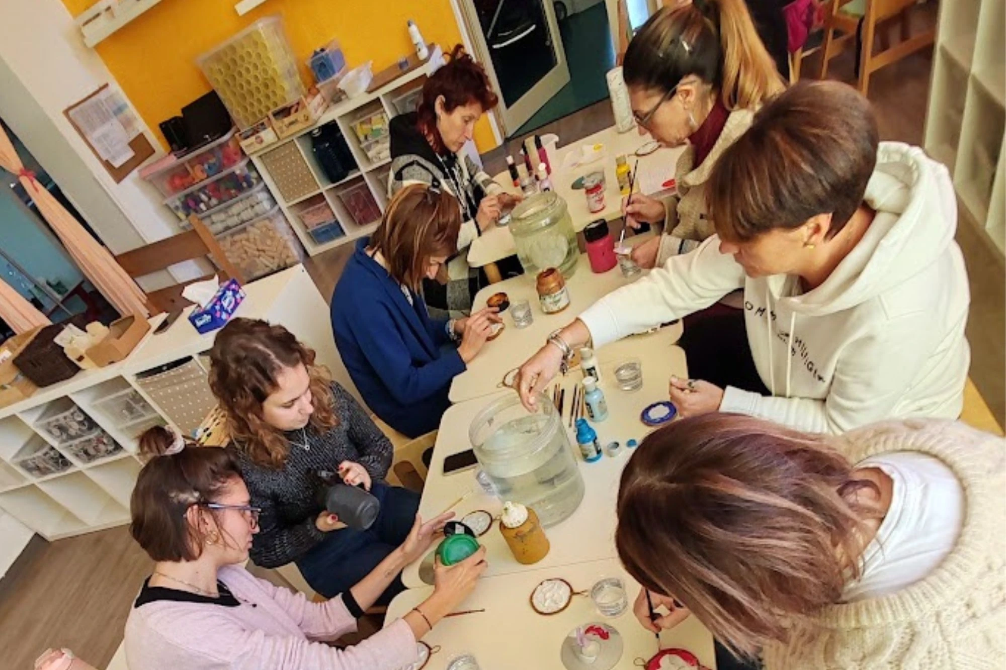 Educatrici sedute attorno a un tavolo lavorano con colori, pennelli e barattoli durante un laboratorio