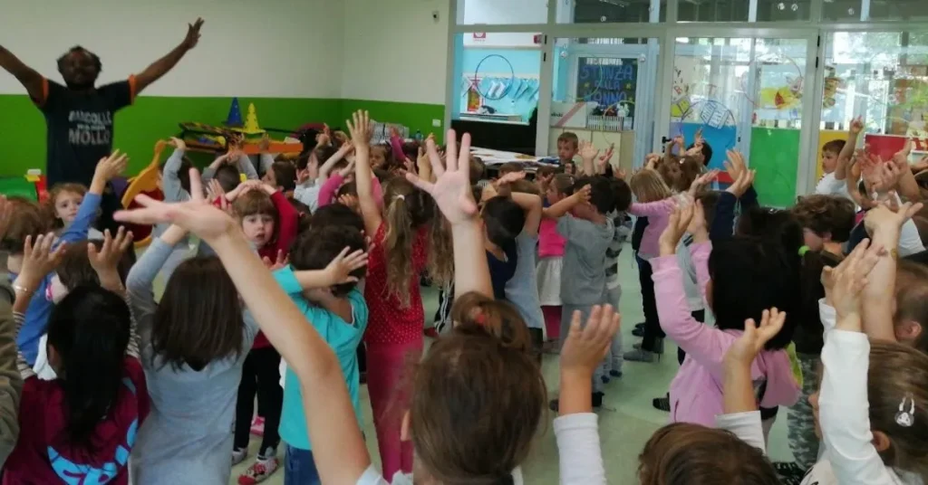 Henri Olama conduce laboratorio con bambini braccia alzate — animatore culturale Bergamo